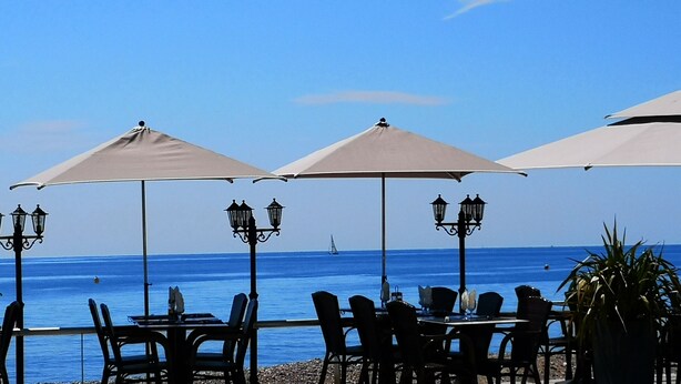 A seaside restaurant with outdoor seating, tables, and umbrellas.