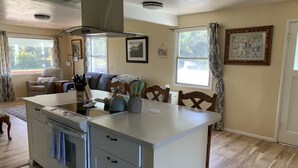 A kitchen with a central island, wooden chairs, a dining table, and a large window.