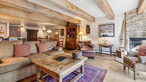 Ein gemütliches Wohnzimmer mit Holzbalkendecke, Kamin, einer Couch, einem Couchtisch und einem gemusterten Teppich.