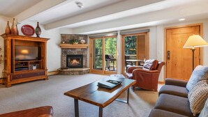 A cozy living room with a fireplace, a wooden entertainment center, a sofa, and a coffee table. - Lodge at Lionshead 204 (Vail)