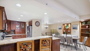A spacious kitchen with wooden cabinets, a marble countertop, and a dining area with a table and chairs. - Lodge at Lionshead 208 (Vail)