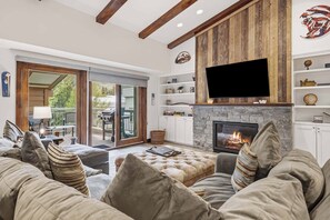 Una sala de estar con chimenea, televisor montado en una pared de madera y un sofá con cojines.