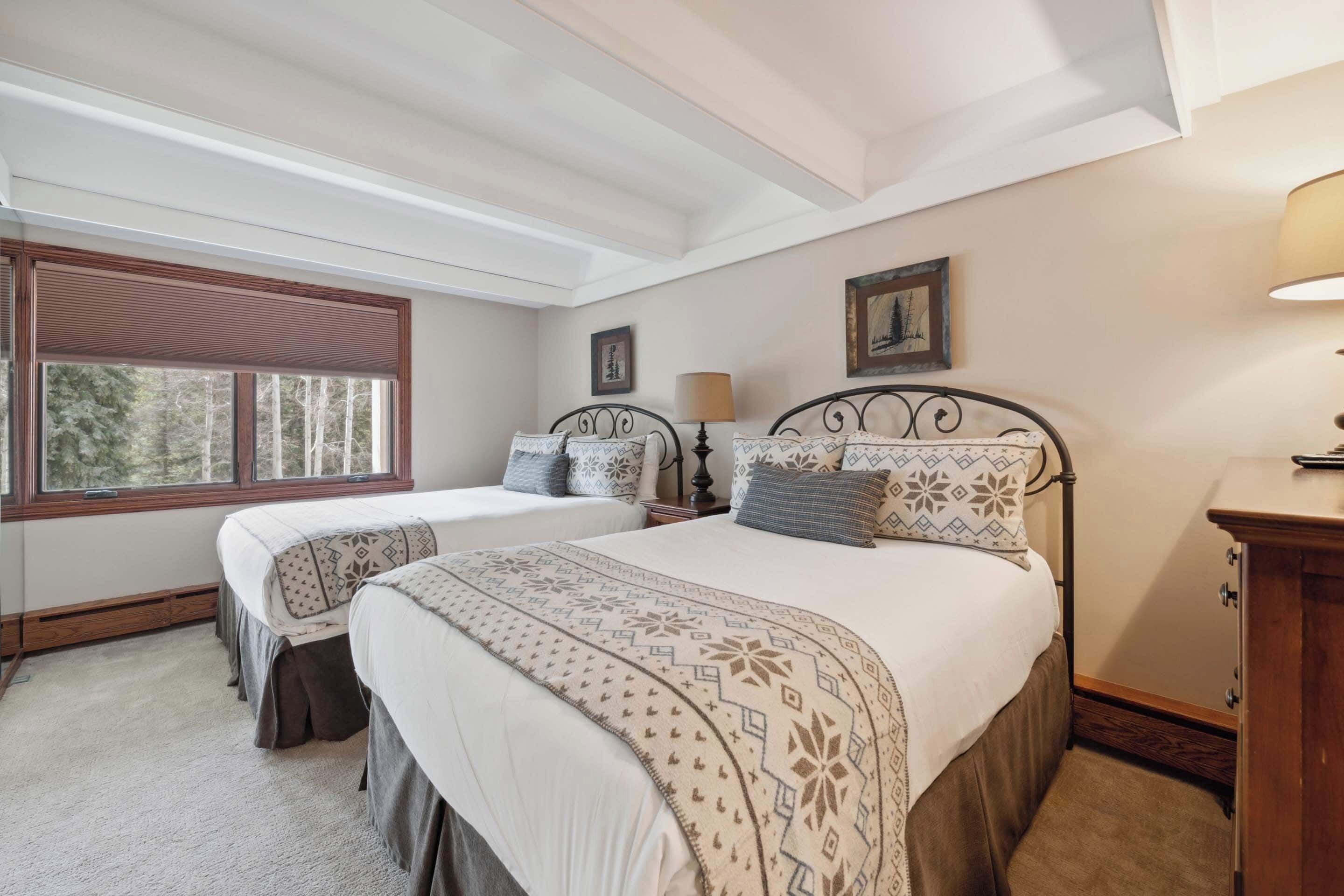 Une chambre avec deux lits, une fenêtre, une lampe et un tableau au mur.