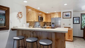 Eine moderne Küche mit Holzausstattung, einem Edelstahlkühlschrank, einer Mikrowelle und einer Bar mit Sitzgelegenheiten.