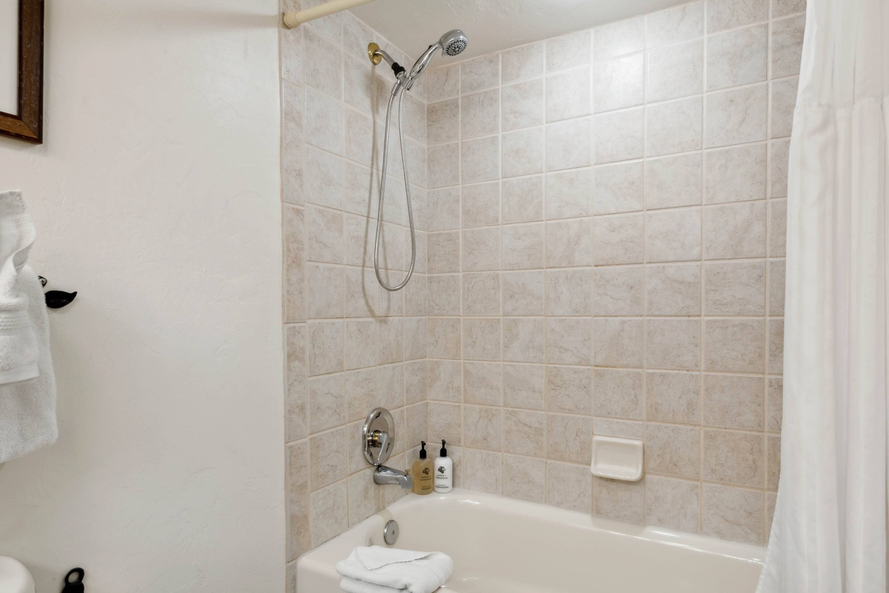 A bathroom with a bathtub, shower, and tiled walls.