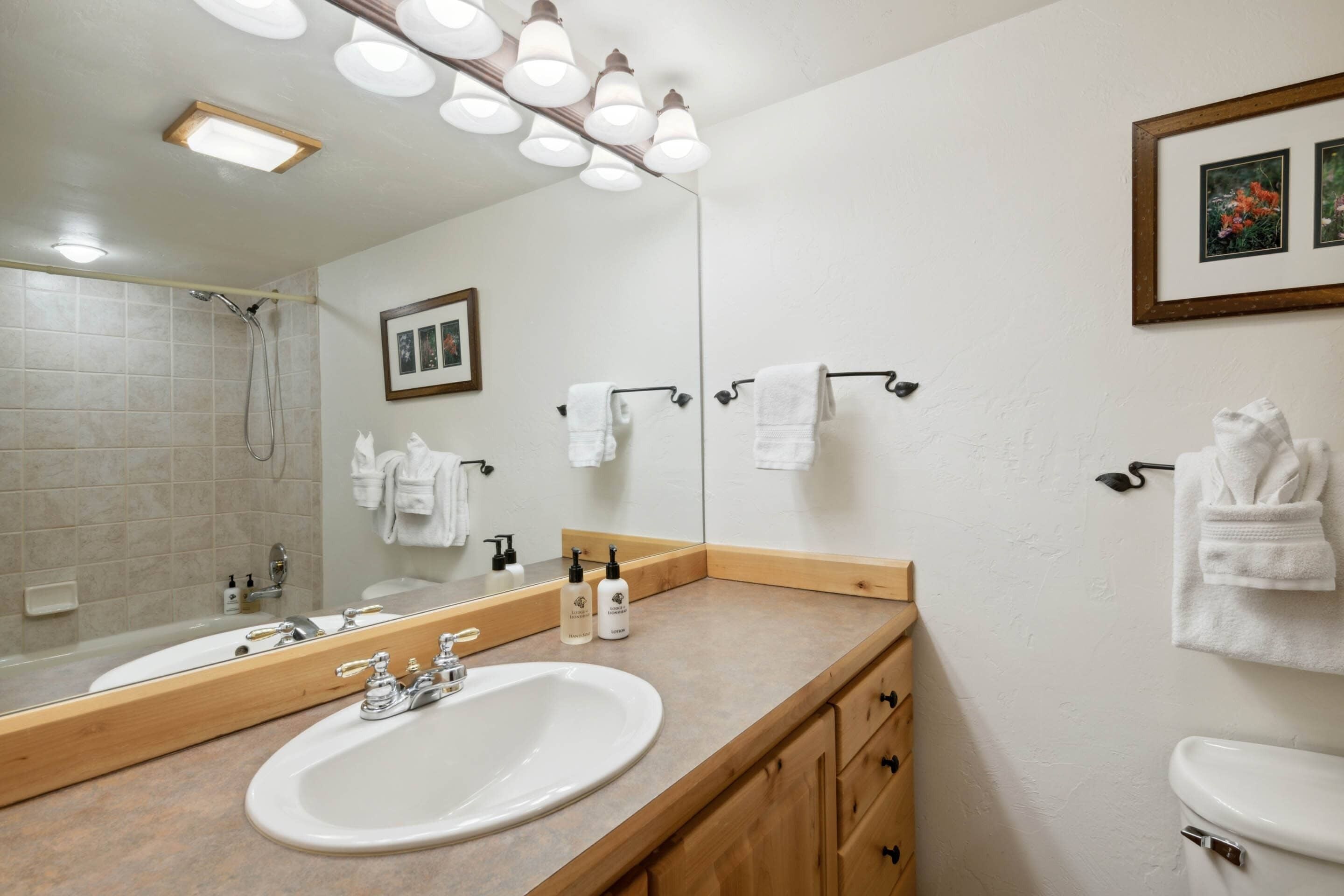 A modern bathroom with a large mirror, two sinks, a shower, and a toilet.