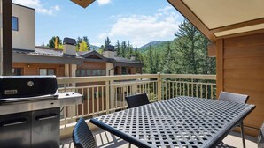 Ein Balkon mit Grill, Tisch und Stühlen mit Blick auf eine gebirgige Landschaft und Gebäude.