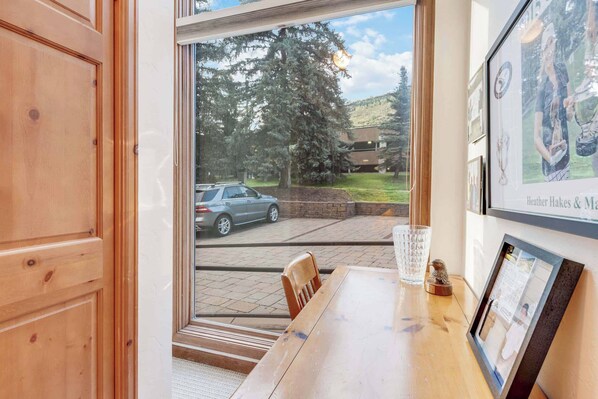 A wooden table with a chair, a glass, and a small figurine in a room with a large window.