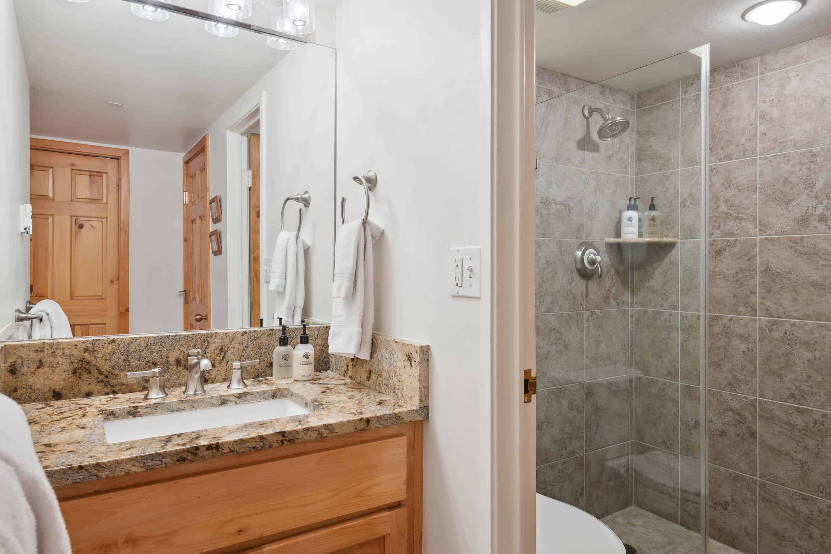 A bathroom with a granite countertop, a sink, and a shower area.