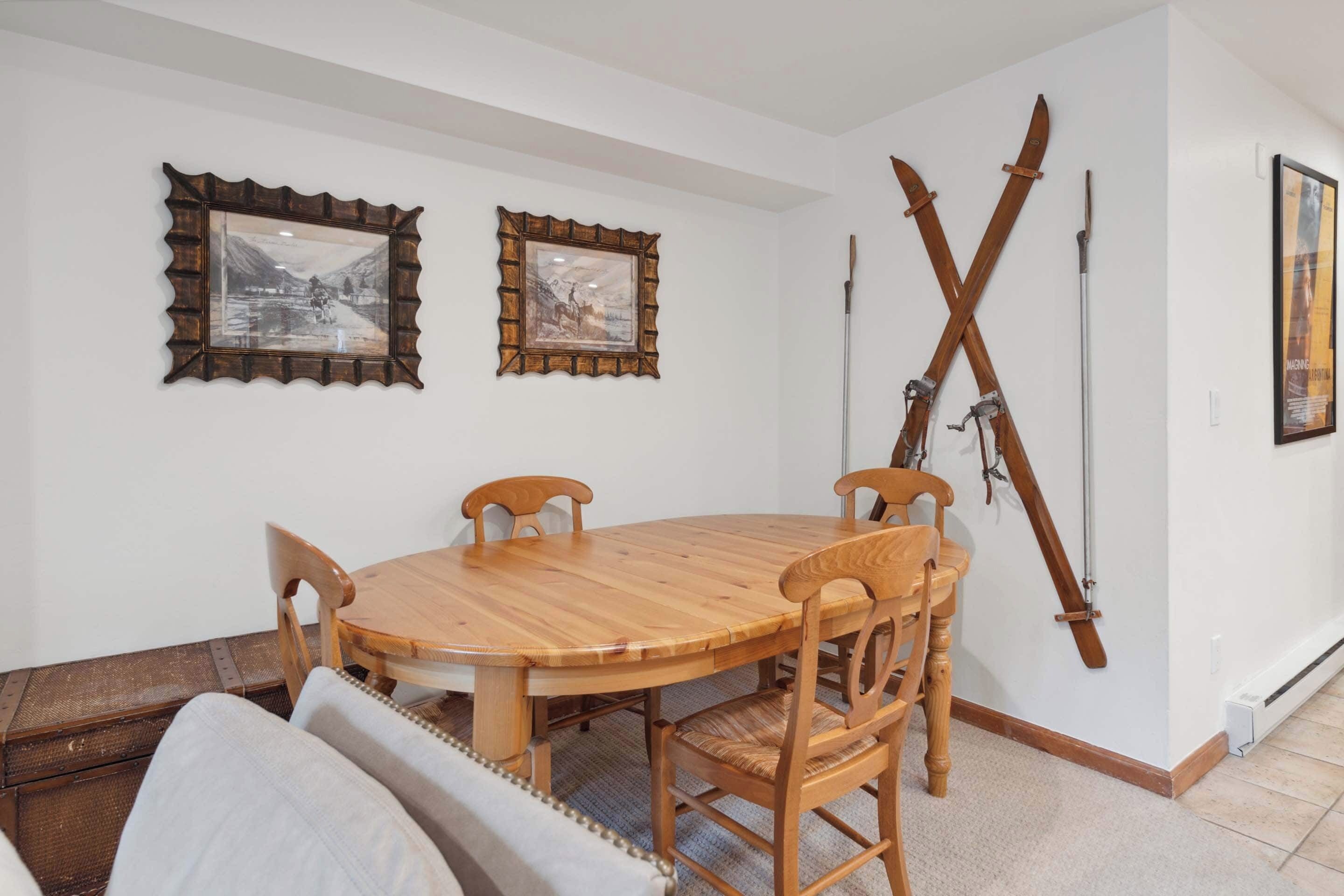 Een eethoek met een houten tafel en stoelen, twee ingelijste foto’s aan de muur, en ski’s die tegen de muur staan.