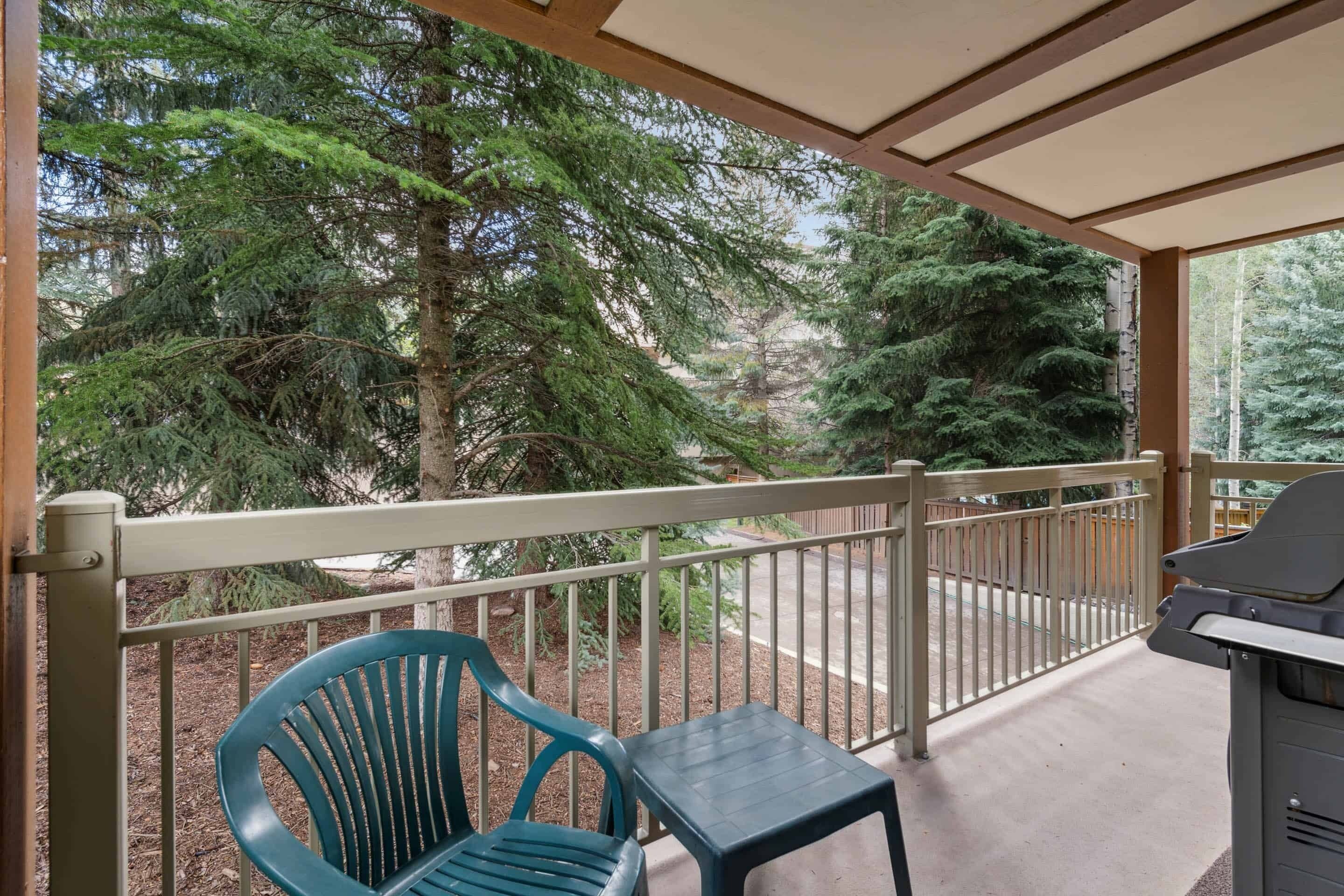 A covered balcony with a grill, a blue chair, and a table.