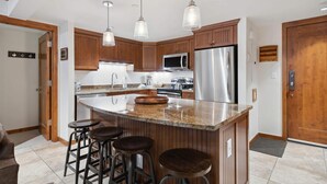 A modern kitchen with wooden cabinets, stainless steel appliances, and a central island with stools. - Lodge at Lionshead 120B (Vail)