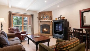 A cozy living room with a fireplace, leather armchairs, a wooden coffee table, and a patterned throw pillow. - Lodge at Lionshead 150A (Vail)