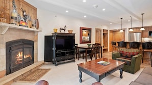 A cozy living room with a fireplace, a television, and a dining area with wooden furniture. - Lodge at Lionshead 150A (Vail)