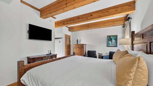 A bedroom with a large bed, wooden ceiling beams, a flat-screen TV, a dresser, and a painting on the wall. - Lodge at Lionshead 160 (Vail)