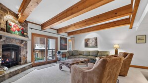 A cozy living room with a stone fireplace, wooden beams, a sofa, and a coffee table. - Lodge at Lionshead 160 (Vail)