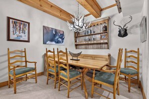 A dining area with a wooden table and chairs, a chandelier, and wall-mounted shelves with various items. - Lodge at Lionshead 160A (Vail)
