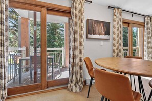 A room with a wooden table and chairs, a painting on the wall, and a sliding glass door leading to an outdoor area with chairs and a table. - Lodge at Lionshead 210 (Vail)