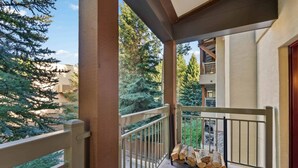 A balcony with a wooden railing, a stack of firewood, and a view of trees and buildings. - Lodge at Lionshead 210A (Vail)