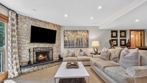 A living room with a stone fireplace, a flat-screen TV, a sofa, and a coffee table. - Lodge at Lionshead 210A (Vail)