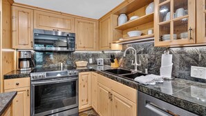 A modern kitchen with wooden cabinets, stainless steel appliances, granite countertops, and a built-in oven. - Lodge at Lionshead 210A (Vail)