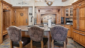 A kitchen with wooden cabinets, a stone floor, and a central island with chairs. - Lodge at Lionshead 230 (Vail)