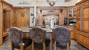 A kitchen with wooden cabinets, a stone floor, and a central island with chairs. - Lodge at Lionshead 230B (Vail)
