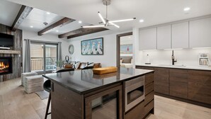 A modern kitchen with a central island, wooden cabinets, and a built-in fireplace. - Lodge at Lionshead 260A (Vail)