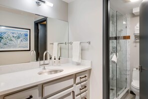 A modern bathroom with a large mirror, a sink, and a glass-enclosed shower.