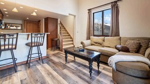 A living room with a sofa, a coffee table, and a kitchen area with a bar stool. - Lodge at Lionshead 340 (Vail)
