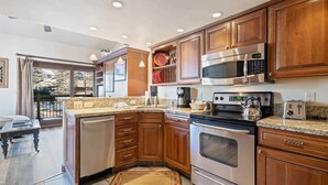 A modern kitchen with wooden cabinets, stainless steel appliances, and a large island with a sink. - Lodge at Lionshead 340 (Vail)