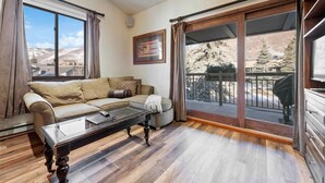 A living room with a sofa, a coffee table, and a large sliding glass door leading to a balcony. - Lodge at Lionshead 340 (Vail)