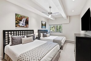 A hotel room with two beds, a ceiling fan, and artwork on the walls.