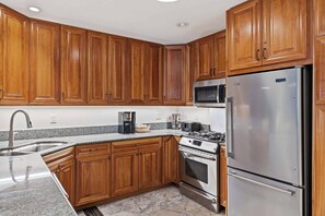A kitchen with wooden cabinets, a stainless steel refrigerator, a microwave, a coffee maker, and a stove. - Lodge at Lionshead 350 (Vail)