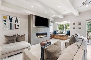 A modern living room with a fireplace, a large flat-screen TV, and a seating area with a sofa and a bench.