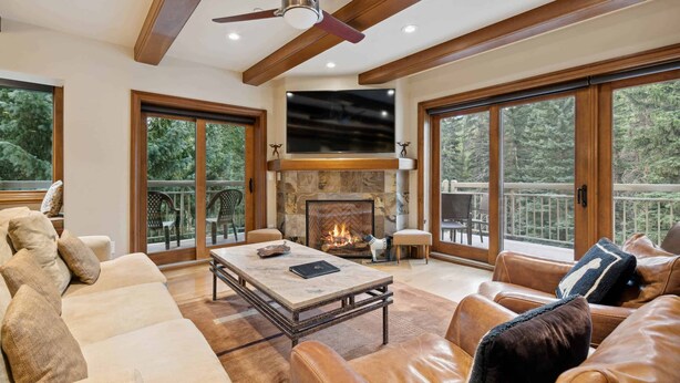 A spacious living room with a fireplace, leather sofas, a coffee table, and large windows offering a view of the outdoors. - Lodge at Lionshead 360 (Vail)
