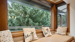 A window seat with three cushions, each featuring a different design, overlooking a dense forest. - Lodge at Lionshead 360 (Vail)