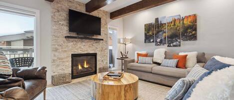 A living room with a fireplace, leather sofas, a round coffee table, and a TV mounted on the wall.