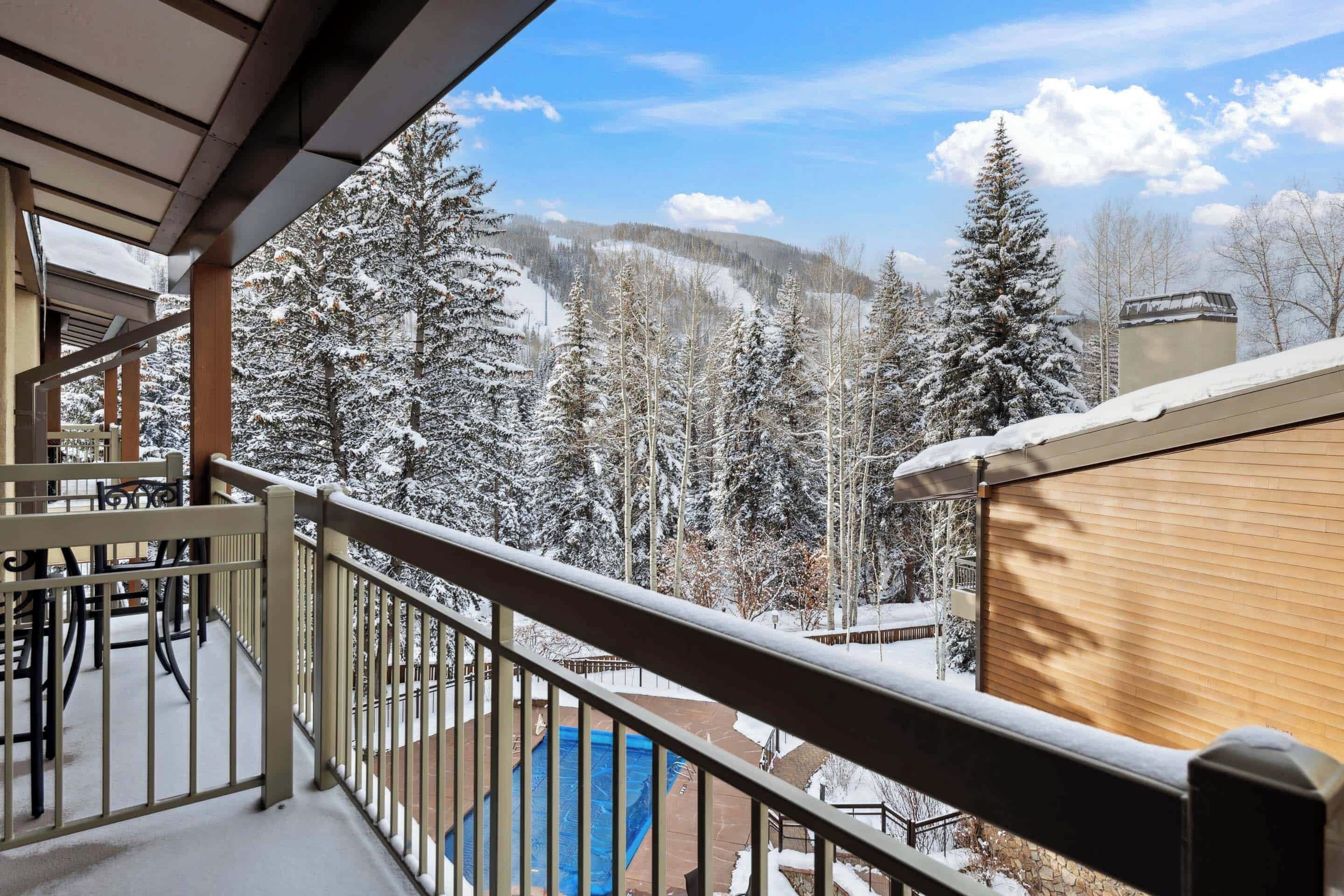 A balcony with a view of snow-covered trees and a mountain range.