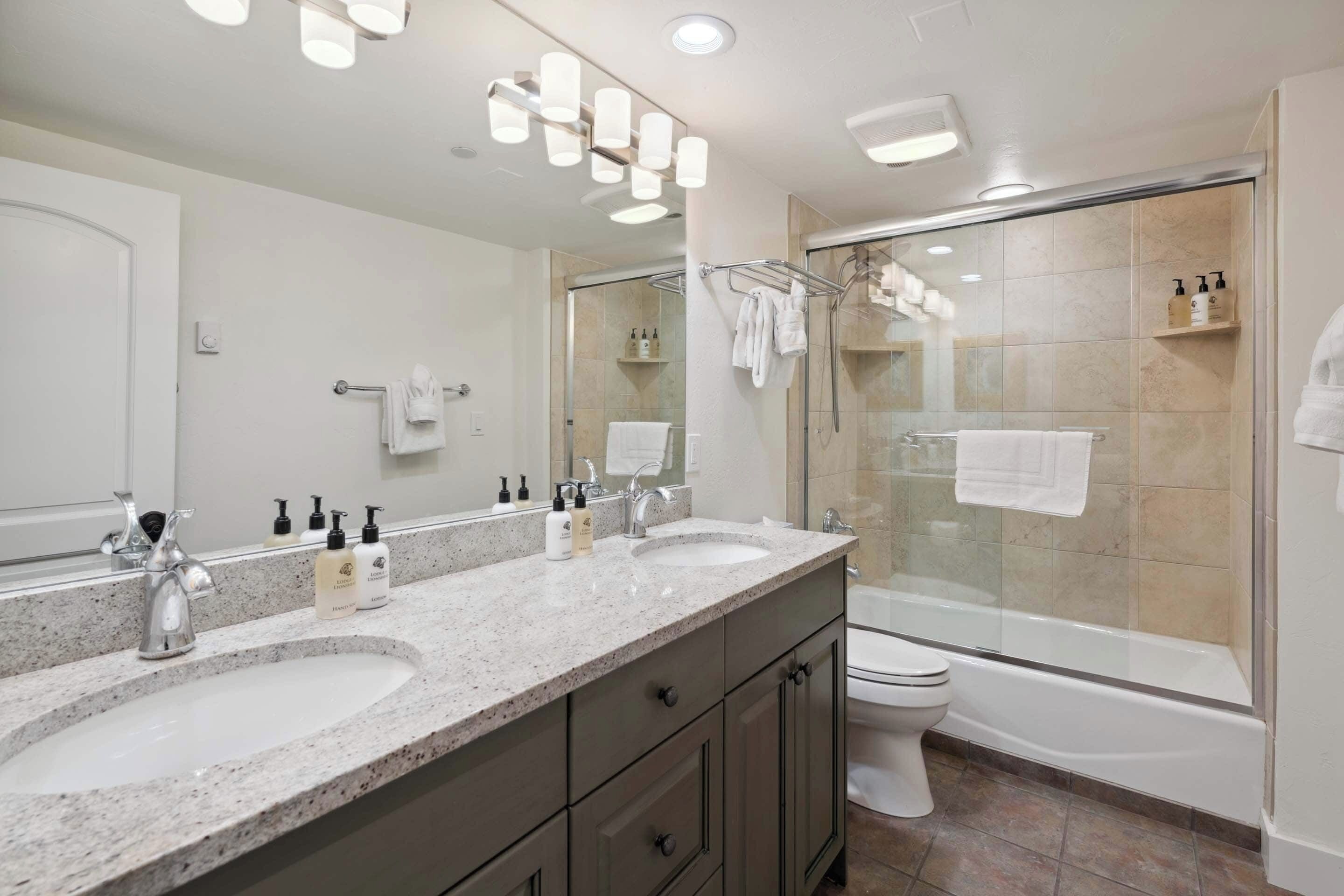 A modern bathroom with two sinks, a toilet, and a glass-enclosed shower.