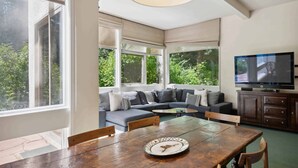 A modern living room with a large window, a sofa, a dining table, and a television. - Lodge at Lionshead 01 (Vail)