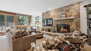 A cozy living room with a stone fireplace, comfortable seating, and a TV mounted on the wall.