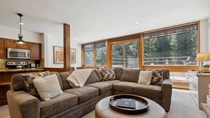 A modern living room with a sectional sofa, a coffee table, and a kitchen area with a microwave and cabinets.
