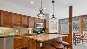 A kitchen with wooden cabinets, a stainless steel dishwasher, a microwave, and a large island with bar stools.