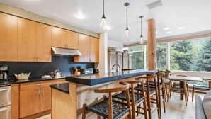 A modern kitchen with wooden cabinets, a black countertop, and a bar area with stools.
