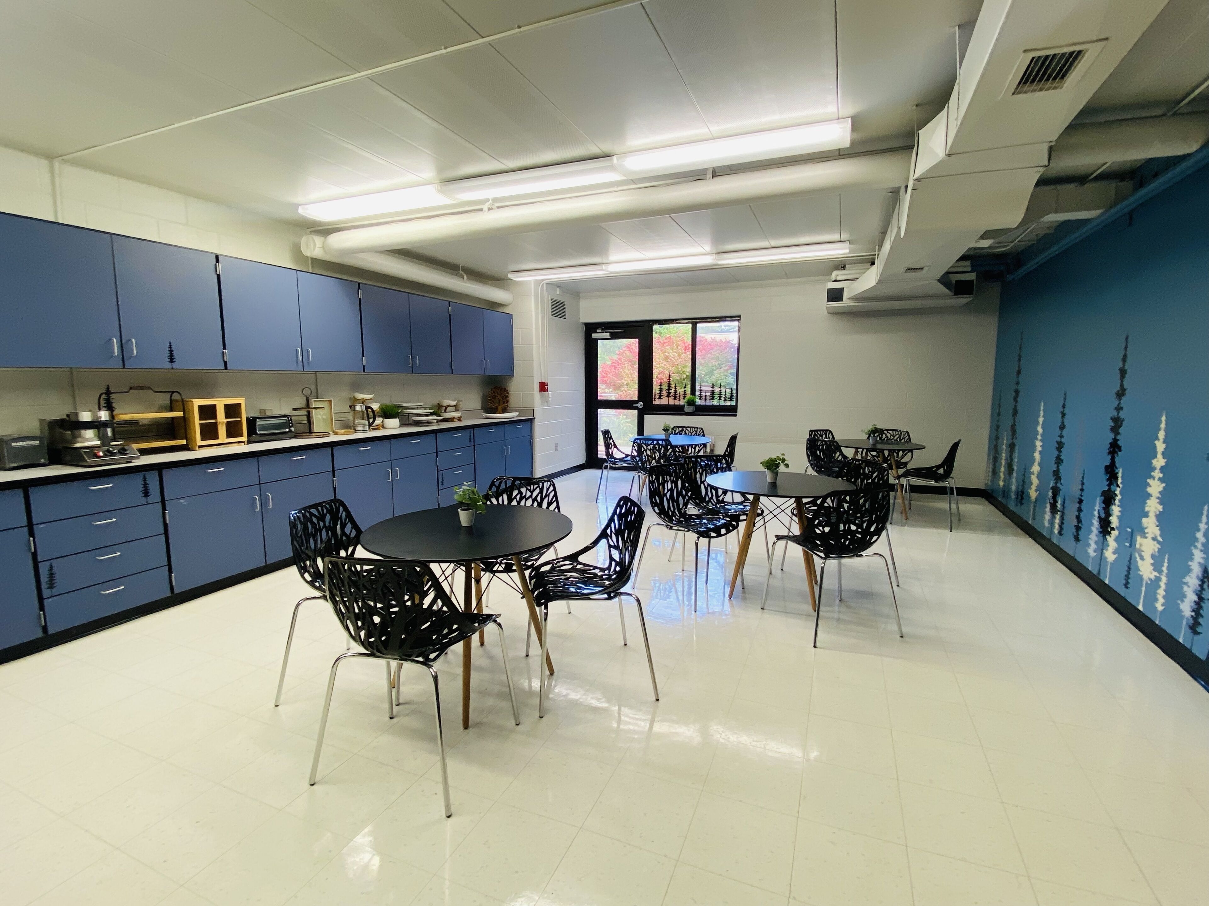 Una cocina moderna con armarios azules y un comedor con sillas y mesas negras.