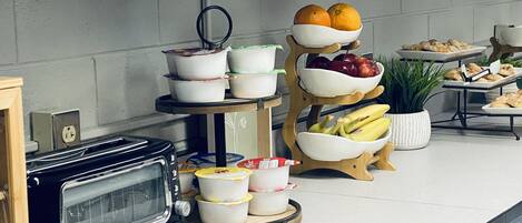 Una encimera de cocina con un tostador, un frutero y una bandeja de pasteles.