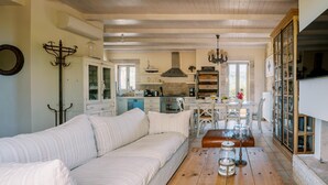 A spacious living area with a sofa, a wooden coffee table, and a kitchen in the background. - Riglia Villas - Villa Olive (West Mani)