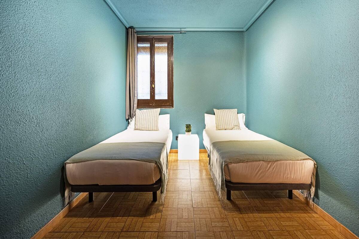 A room with two beds, a small table, and a window with curtains.