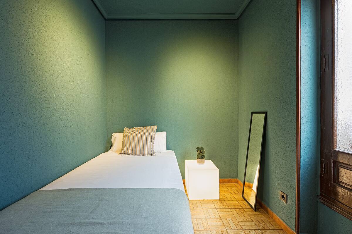 A bedroom with a bed, a nightstand, a mirror, and a window.
